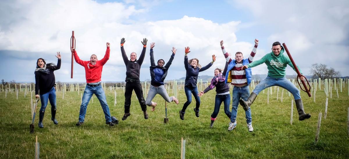 Group of corporate volunteers leaping the air in a tree planting field 