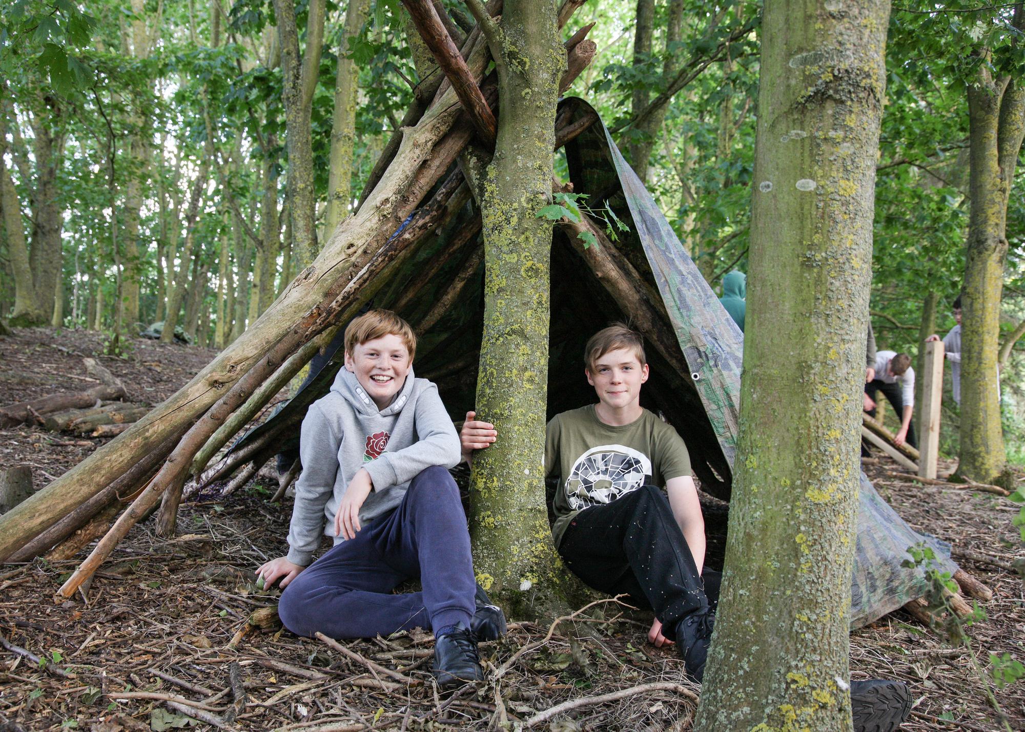 Two young people sitting in front of a den they have built in the Forest