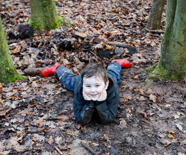 A child lay on his front in the woods having fun at Mini Foresters