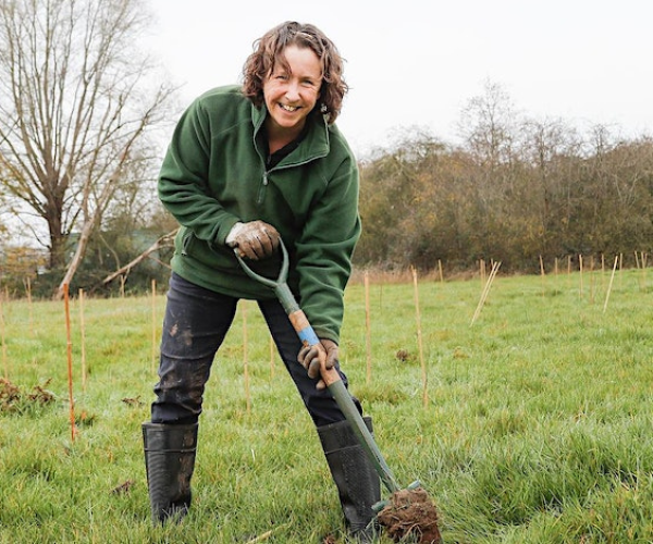 A volunteer smiling whilst digging a hole during a tree planting activity session.