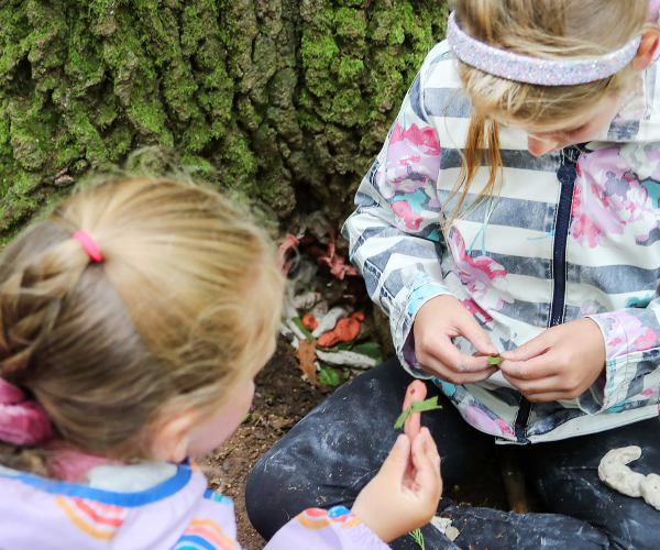 A couple of children doing crafts in the woods together on the Forest floor