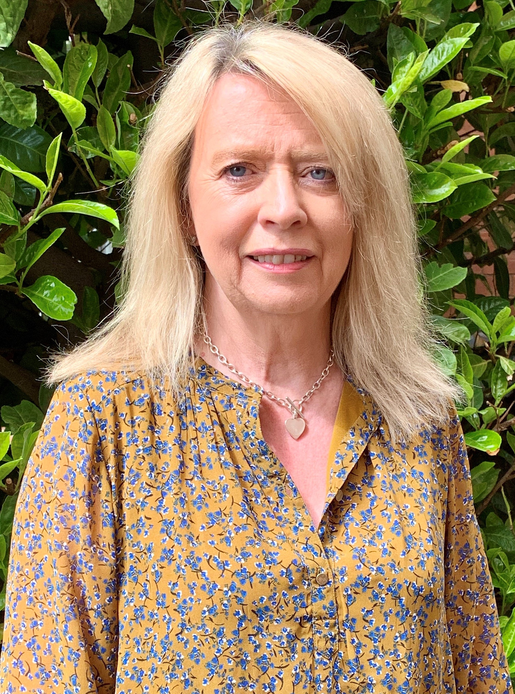 Doreen Massey standing outside with green leaves behind her