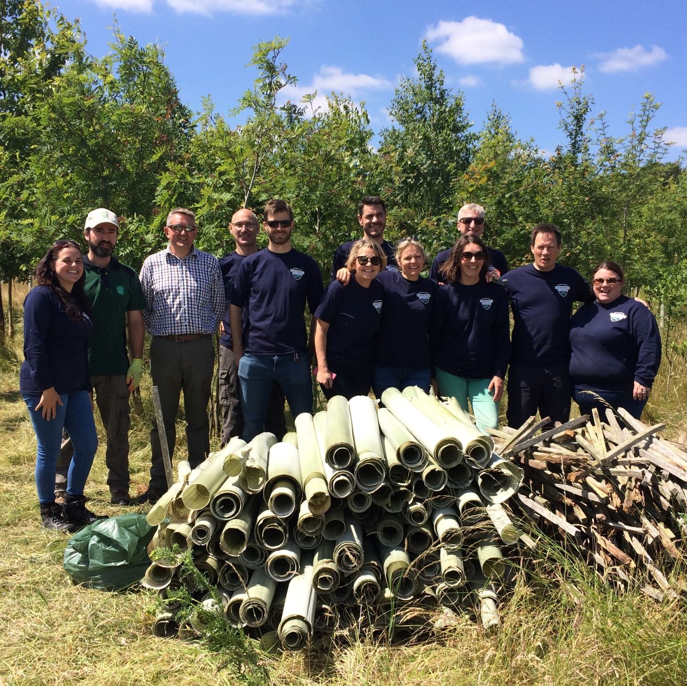 Corporate group stood behind pile of tree tubes and stakes they have removed from the Forest