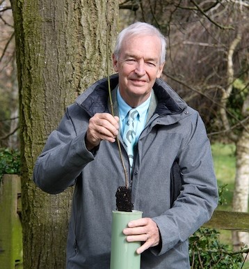 Head and shoulders photo of Jon Snow, Chair of trustees, holding a tree sapling