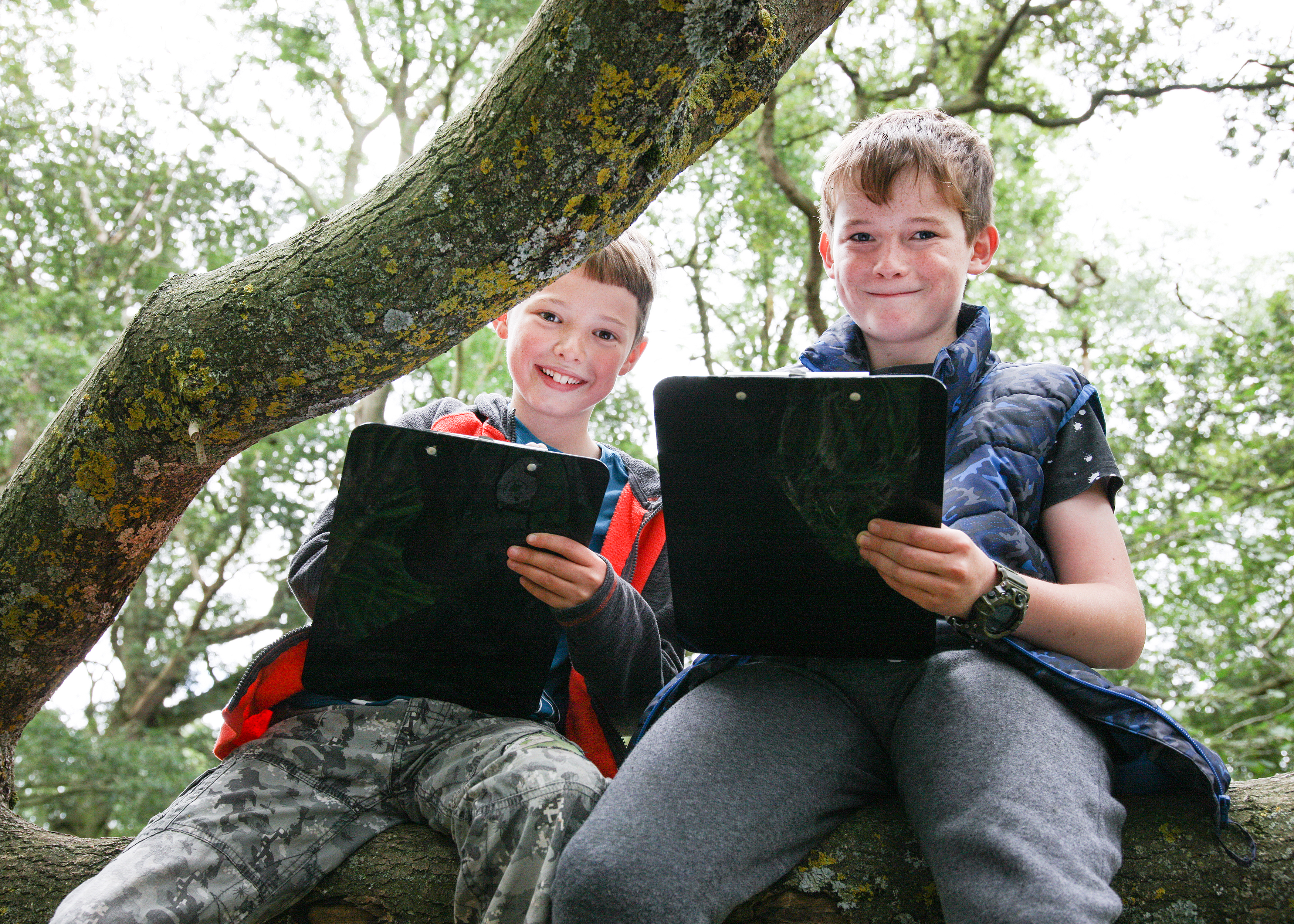 Two young foresters sitting on a tree trunk with clipboards