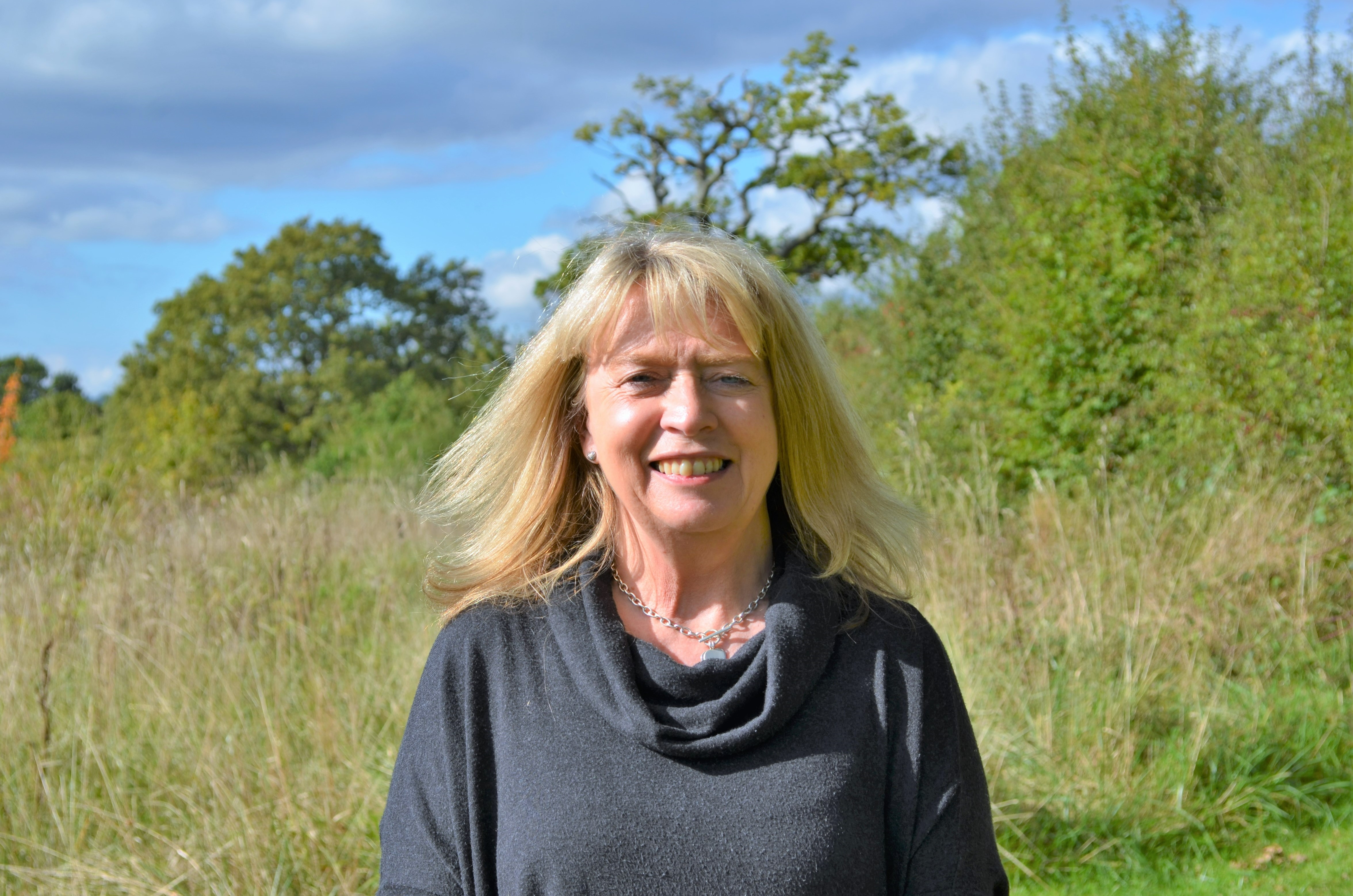 Doreen smiling in front of a green wildflower meadow