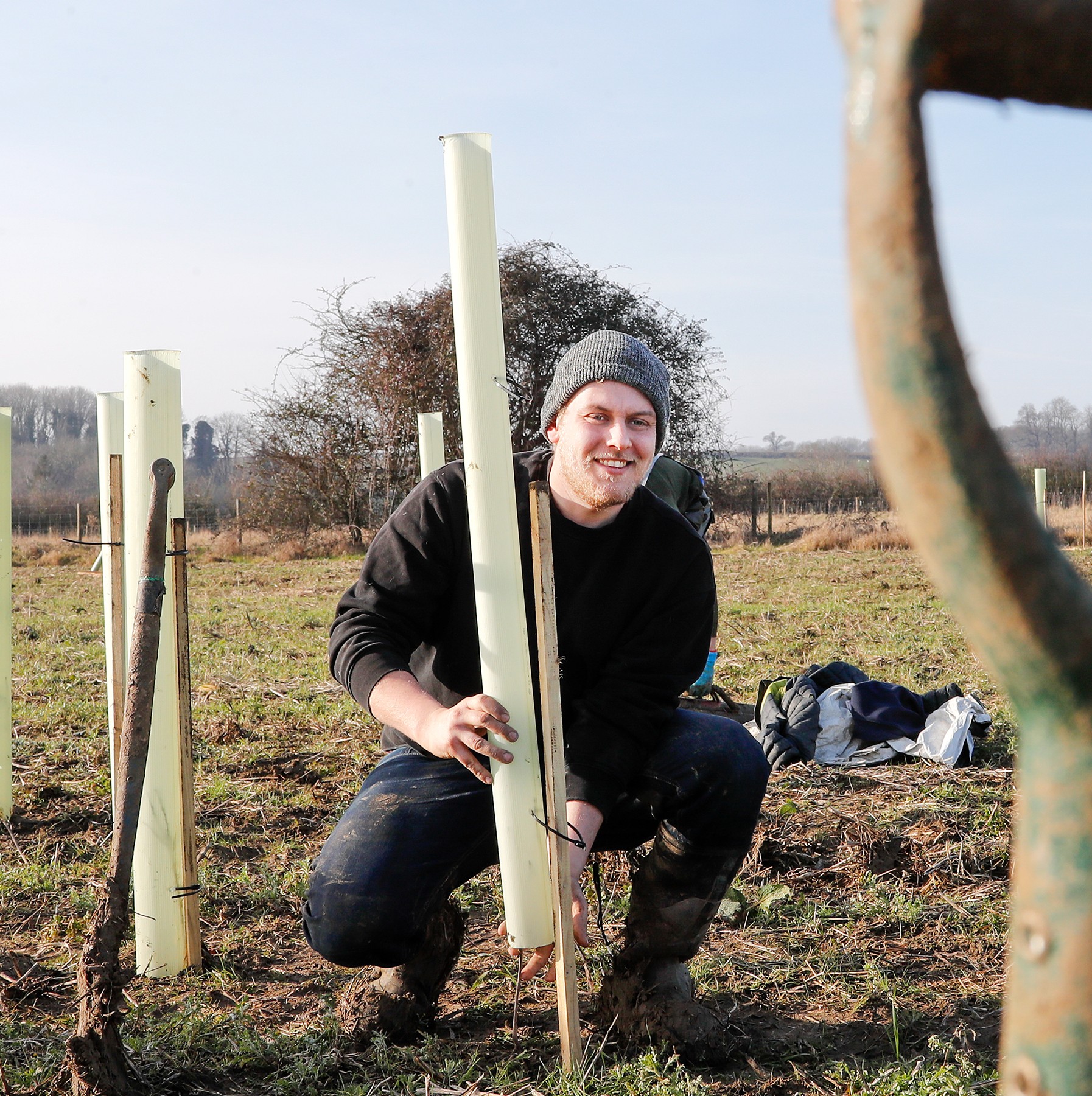 A photograph of James planting a tree and smiling at the camera