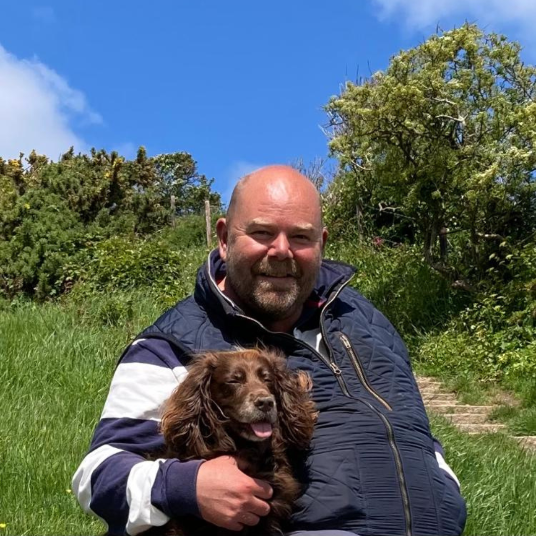 Simon Theobald smiling at the camera with his dog next to him in the Forest