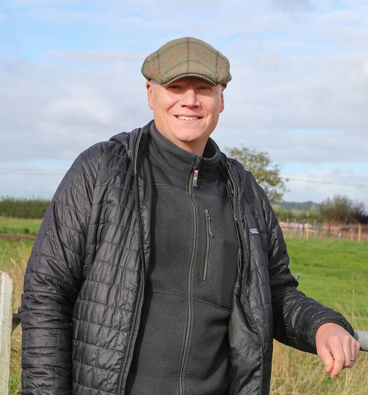 A photo of Tom Davies smiling at the camera, leaning on a post.