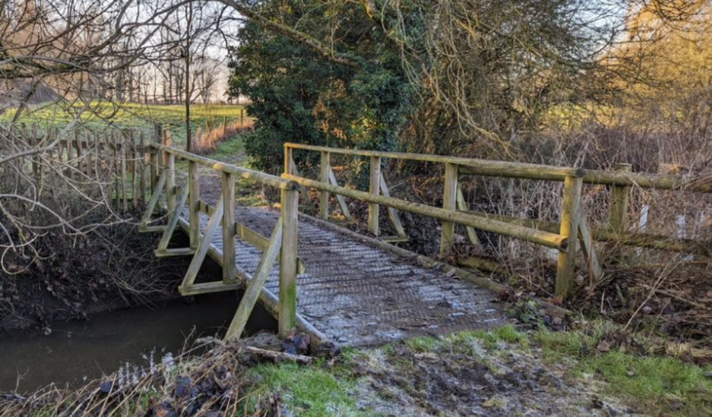 A pathway crossing a wooden bridge surrounded by mature trees