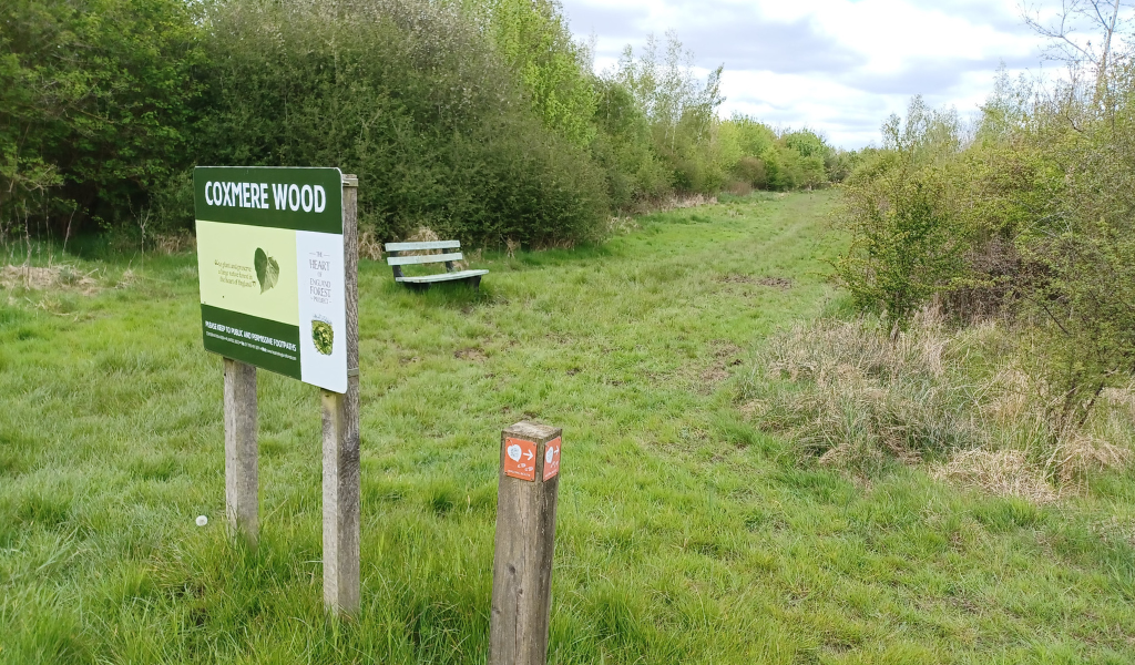 A bench and another Coxmere Wood sign along the footpath