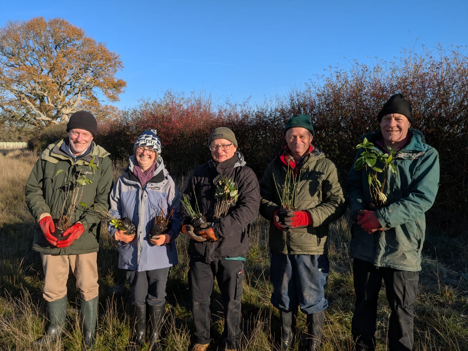 A row of volunteers holding tree saplings in their hands smiling at the camera 