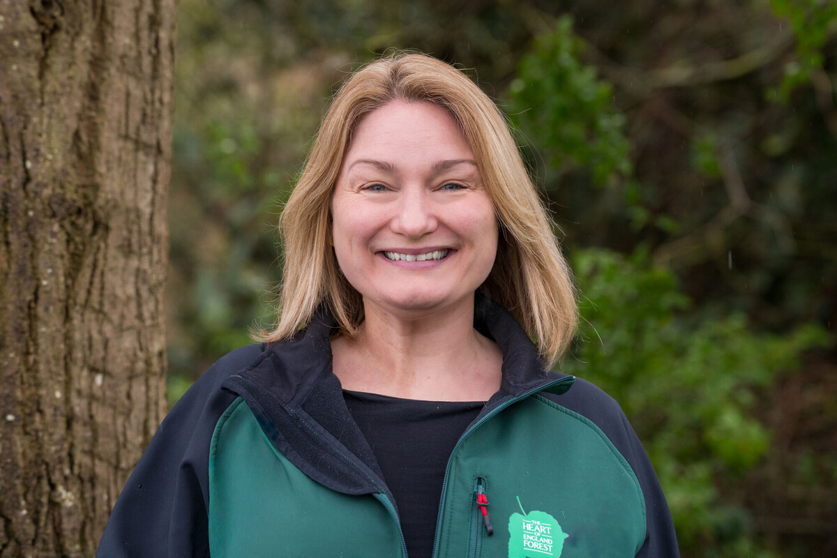 A head and shoulders shot of Catherine Chatterton in a green branded jacket for the Heart of England Forest smiling at the camera