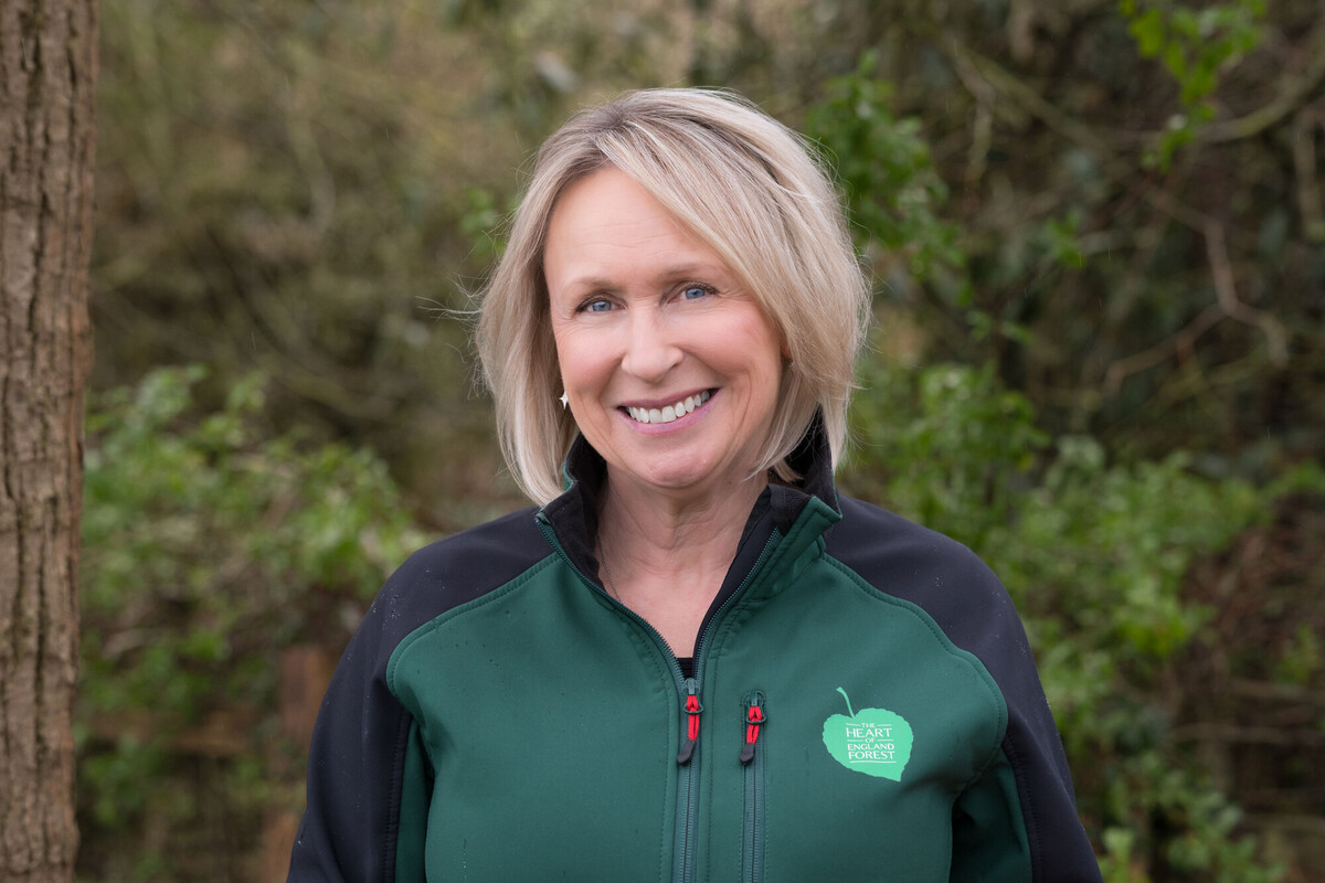 Julie Blakemore smiling at the camera, wearing a branded jacket, with a green hedgerow in the background