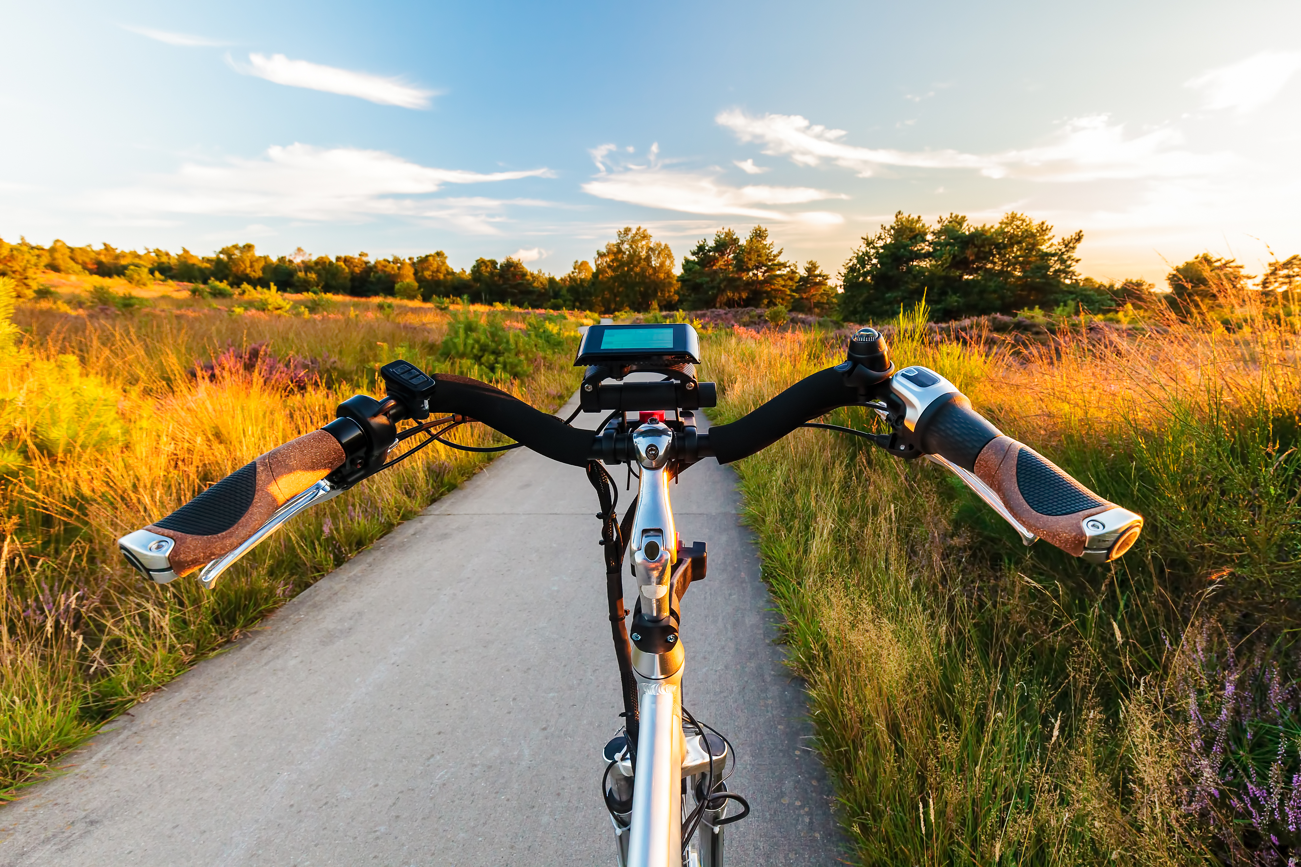 Close up of the handlebars of a bicycle as it moves down a straight road with a grassy field on either side.