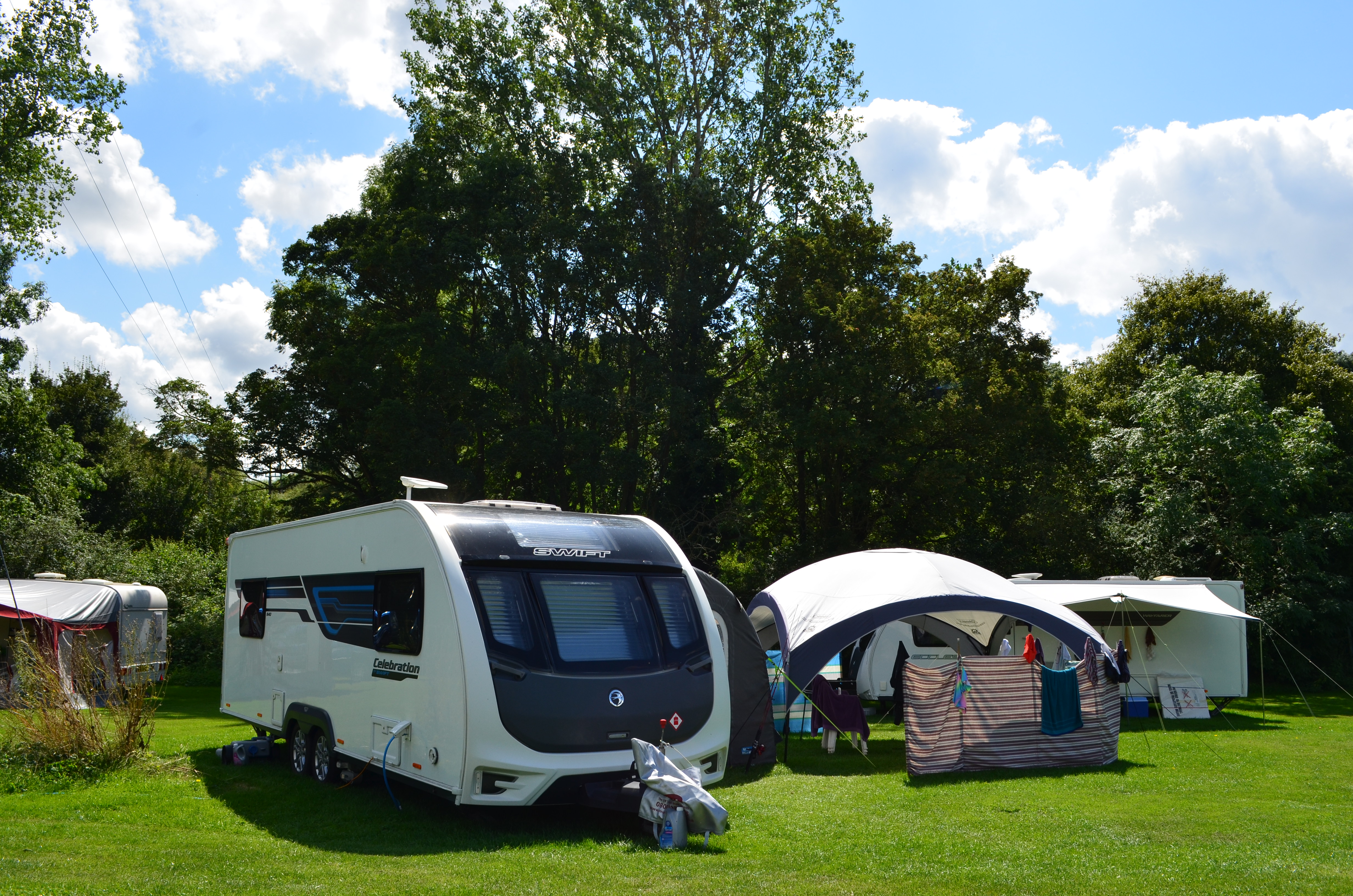 A caravan and tent pitched on a grassy area in front of some mature trees