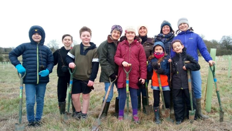 Group of adults and childreb wrapped up warm, some holding spades, at a community tree planting session in Bearley