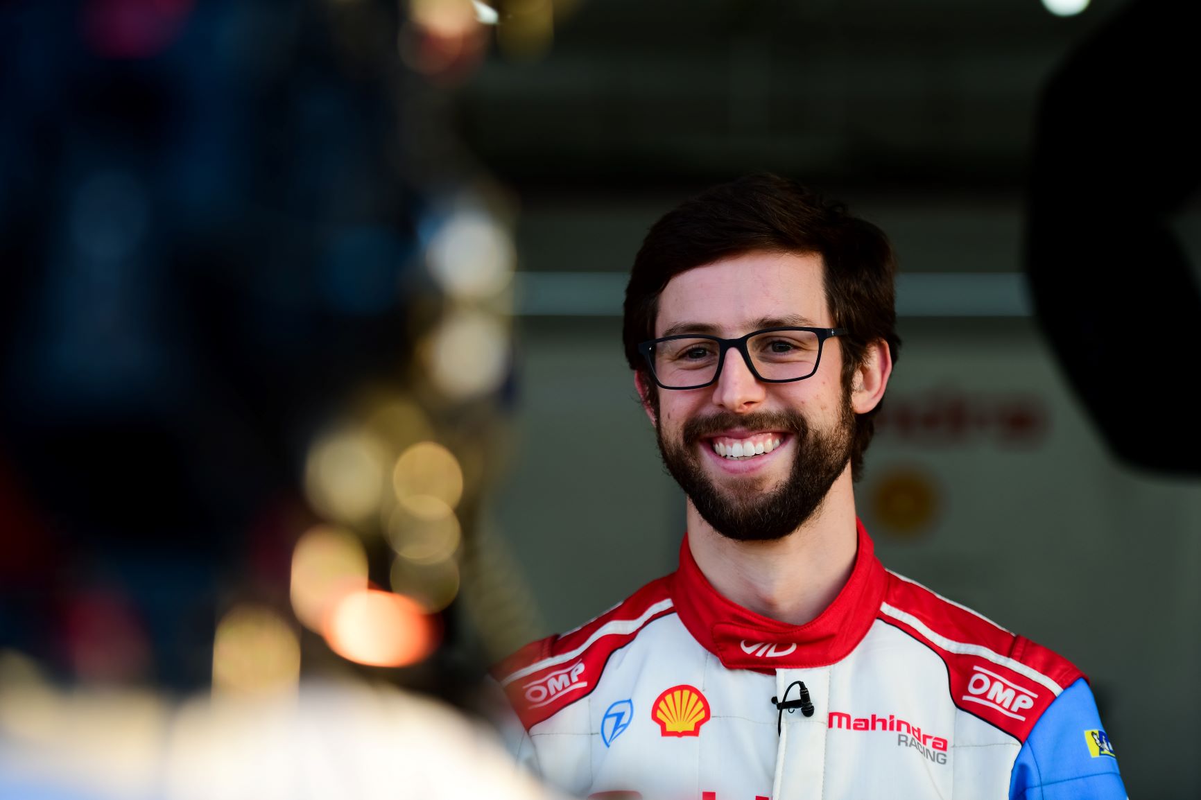 Head and shoulders photo of Alexander Sims standing smiling in his racing suit