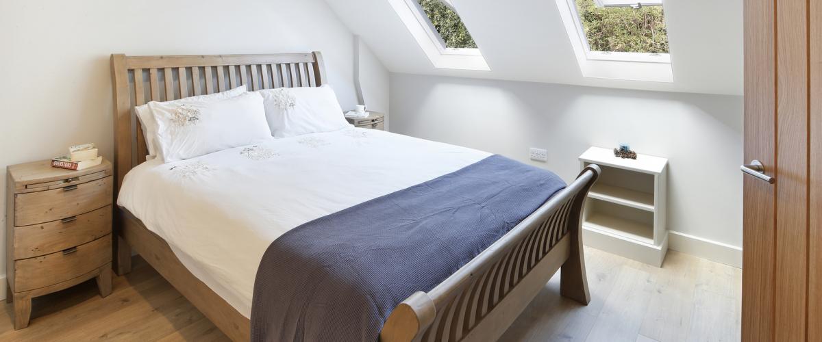 A double bed with white sheets in the middle of a bedroom in Oak Cottage. Two sky light windows let light in through roof on right hand side.