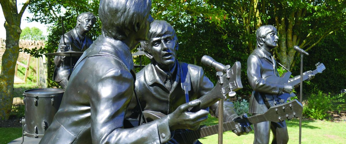 Close up of bronze statues of The Beatles playing instruments and singing into microphones 