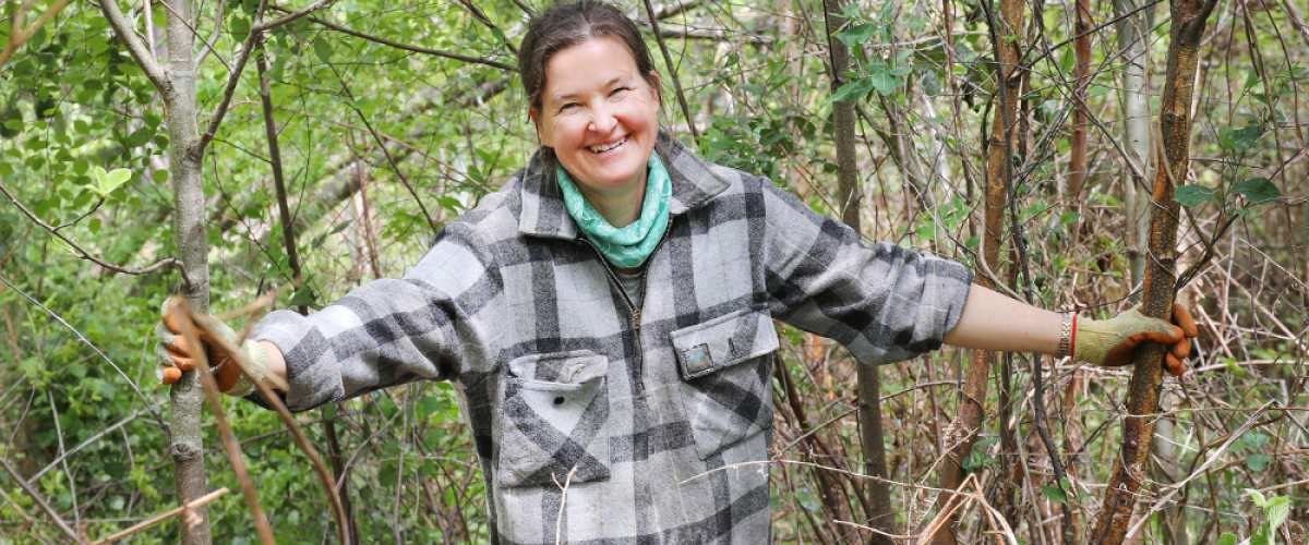 A female volunteer smiling, holding onto two trees either side of her