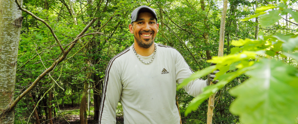 Leo, a volunteer smiling while standing in a native broadleaf woodland setting in the summer