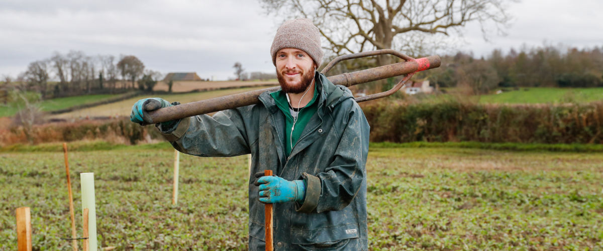 An apprentice holding a stake basher whilst tree planting.