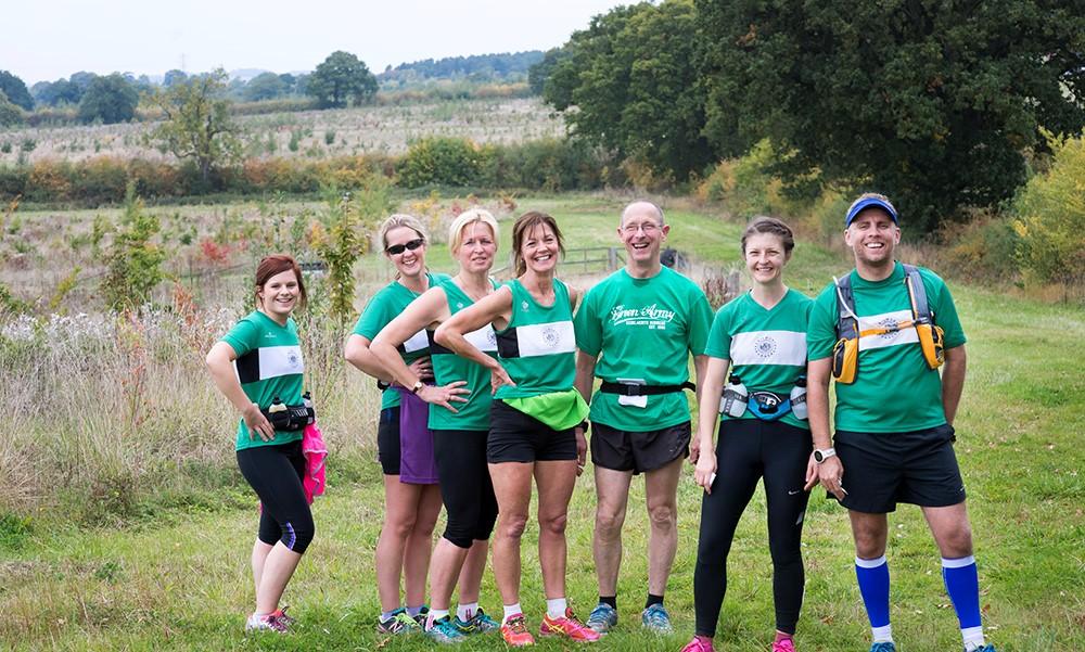 Group of 6 runners in kit standing in a forest ride in front of mature trees