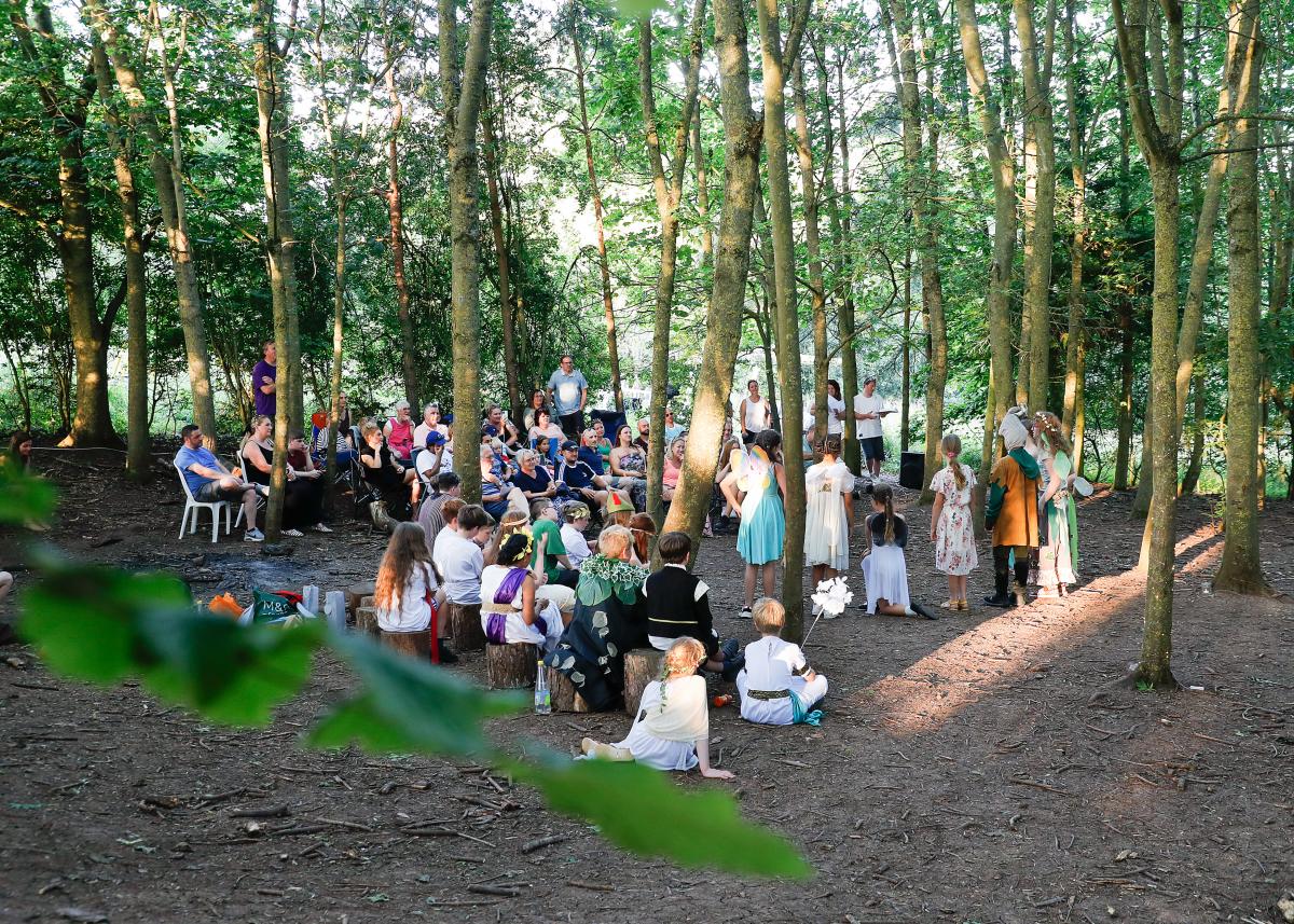 Parents gather to watch the school pupils performing in a Forest clearing surrounded by tall trees