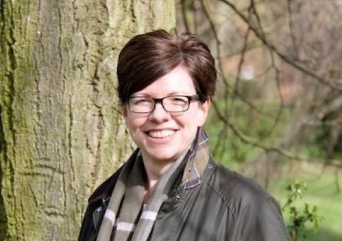 Portrait photo of Alison smiling in front of a tree trunk