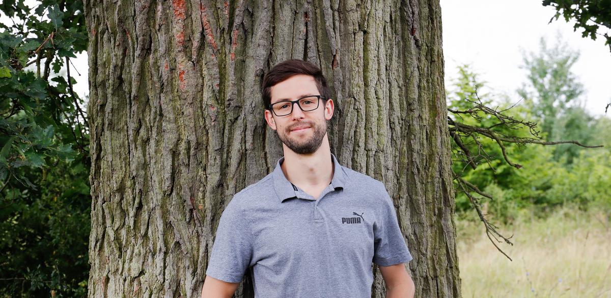 Alexander leaning on a tree trunk, smiling at the camera.