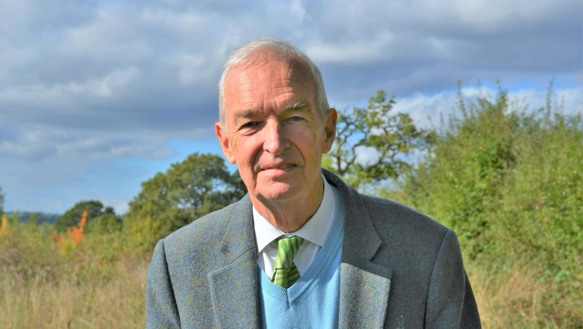 Jon Snow in a suit and tie with grass and trees in the background