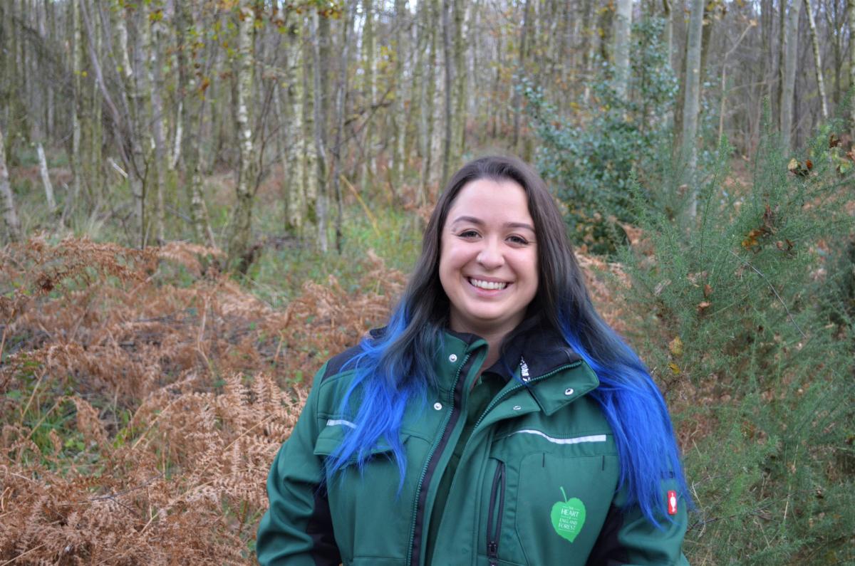 Head and shoulders shot of Tasha smiling at the camera wearing a branded jacket and standing in front of some autumnal coloured scrub