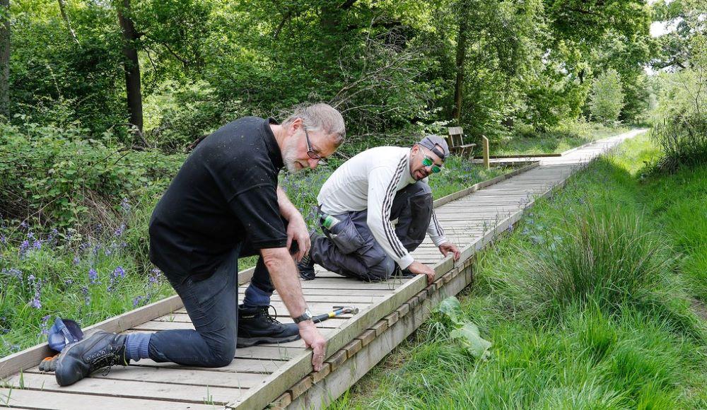 Two male volunteers kneeling on the boardwalk on our accessible trail fixing a side board