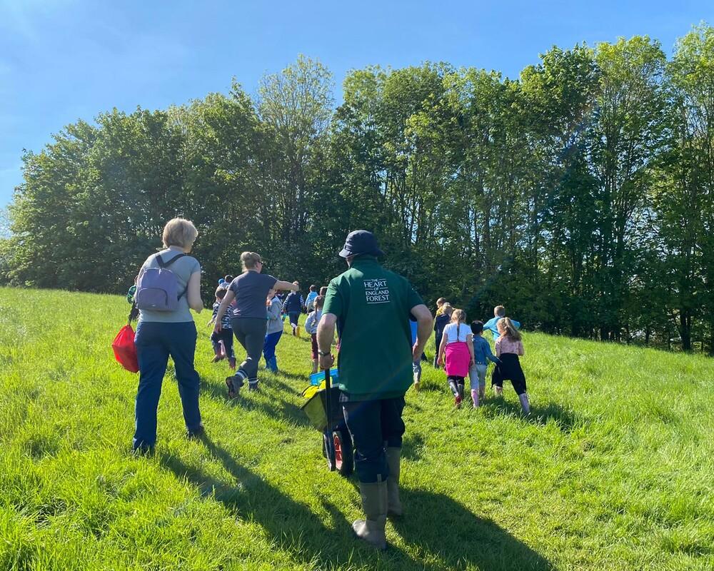 Outdoor Teacher Phil walking a class of primary school students up a hill to the outdoor learning space in the woods