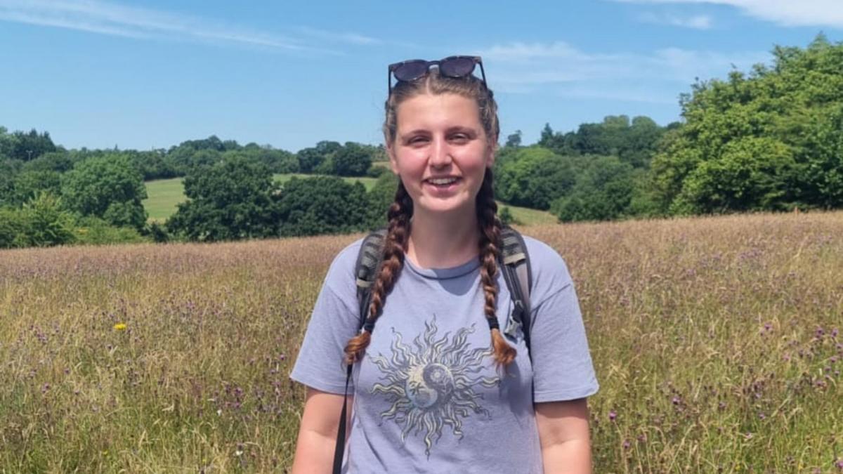 Becky, Biodiversity Intern, standing in a field with trees in the background. 