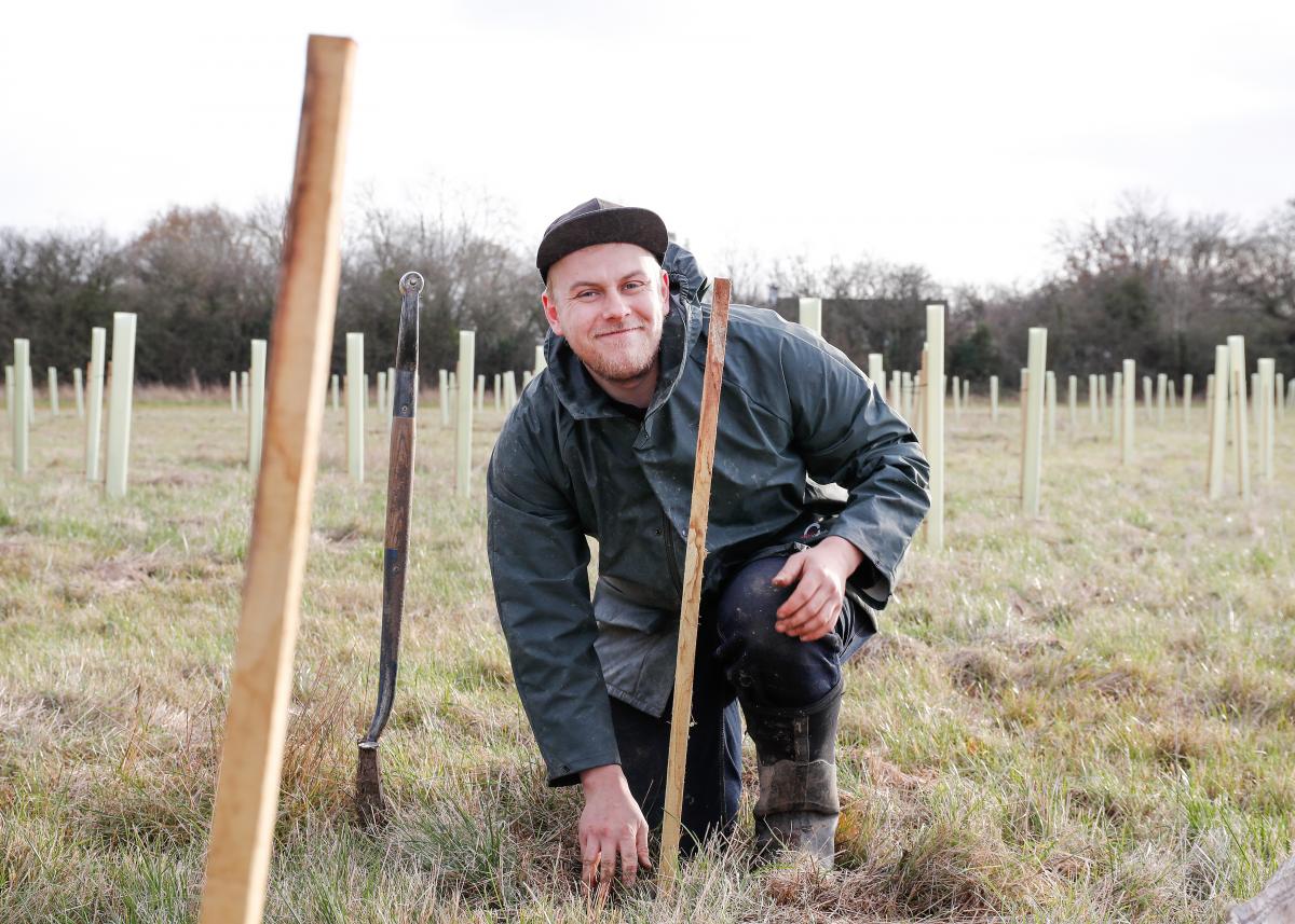 Senior Forest Ranger James crouching down smiling at the camera whilst tree planting