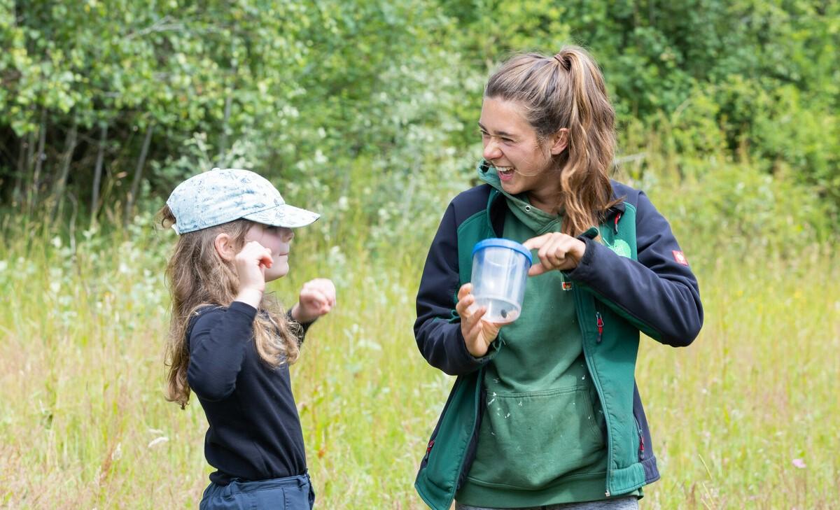 Forest Ranger Phoebe looking into a bug catcher and smiling with a young girl