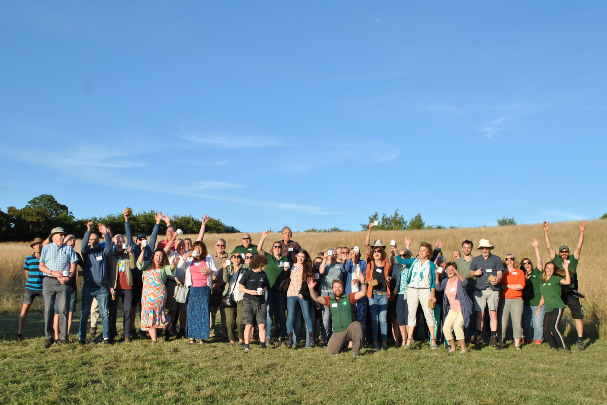 A group of volunteers, volunteer leaders and staff with their arms up in the air on a summer evening at Middle Spernal