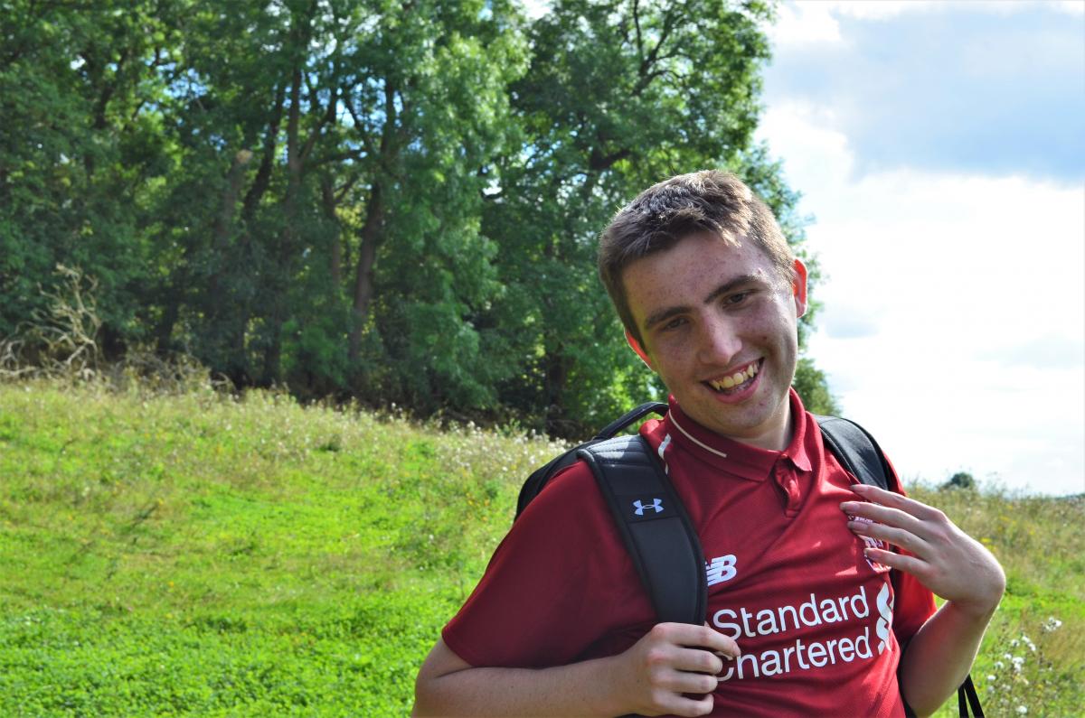 A close up of supported intern Tom standing in the Forest and smiling at the camera