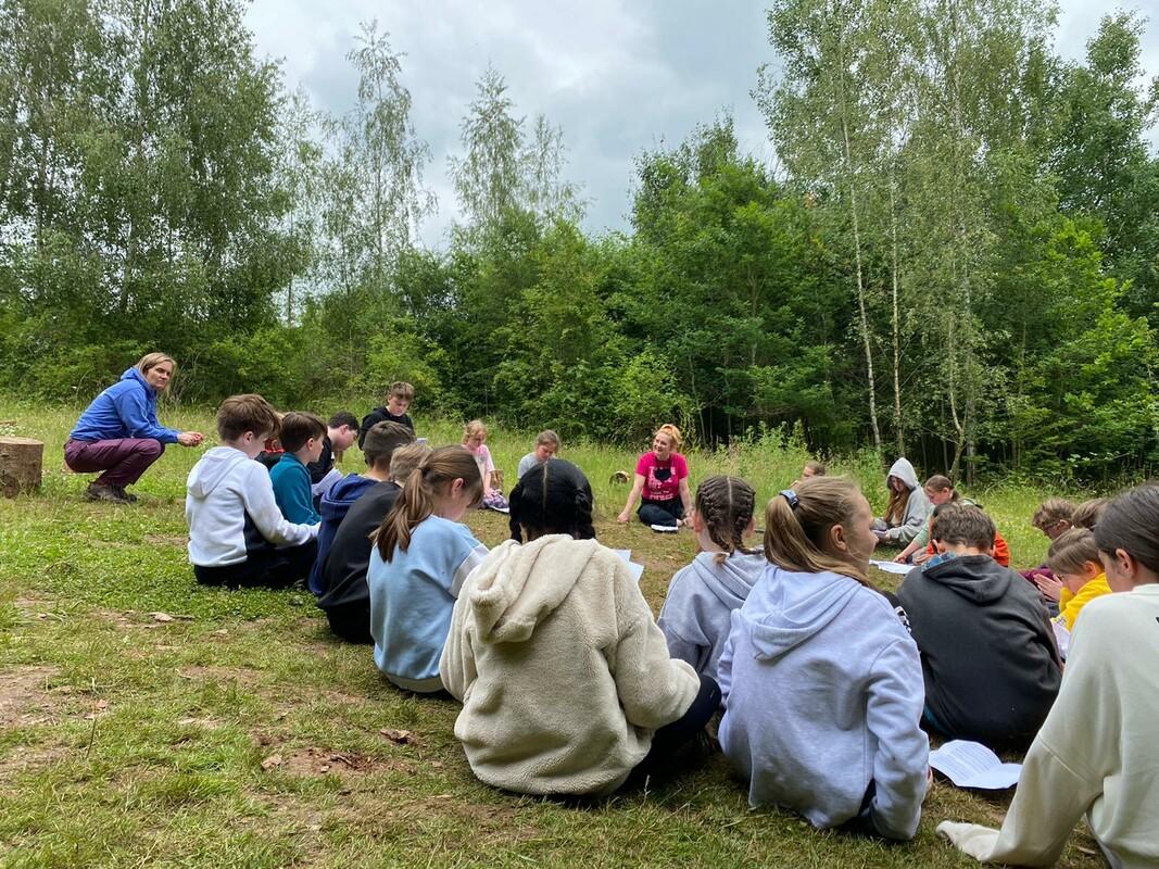 A group of pupils from Mappleborough Green Primary School sitting in a circle on the grass surrounded by woodlands