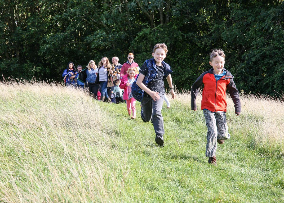 Young children running down the hill, adults watching from the entrance of the wildwood