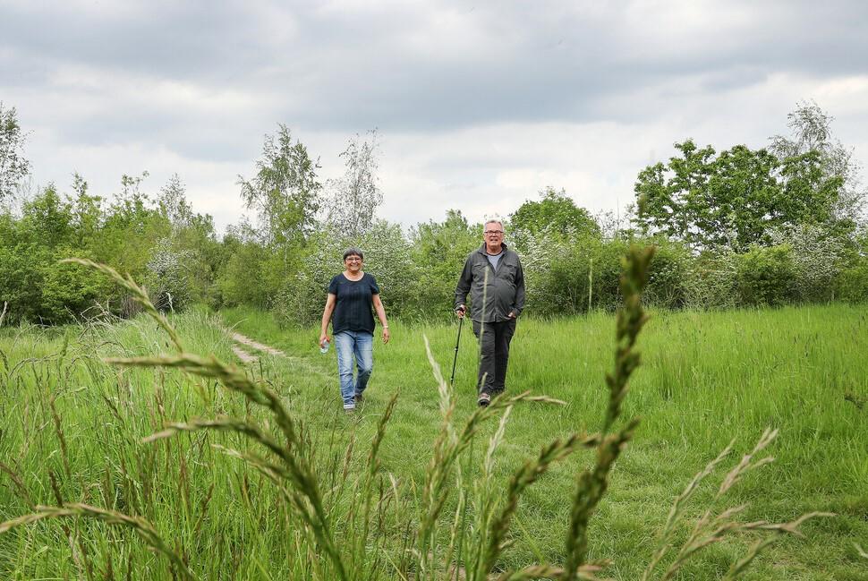 A male and female walking on a footpath through an open area of the Forest with grasses in the foreground