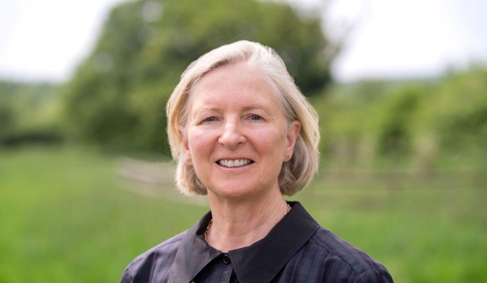 A head and shoulders photo of Heather Acton taken with grass and trees in the background. Heather is smiling at the camera