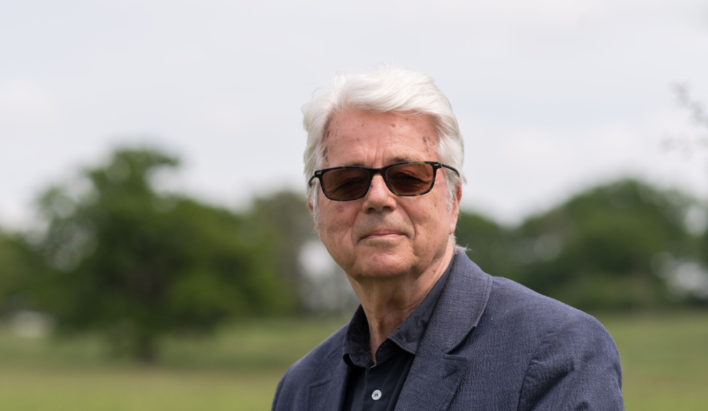 A head and shoulders photo of Anthony Burton CBE taken with grass and trees in the background. Heather is smiling at the camera