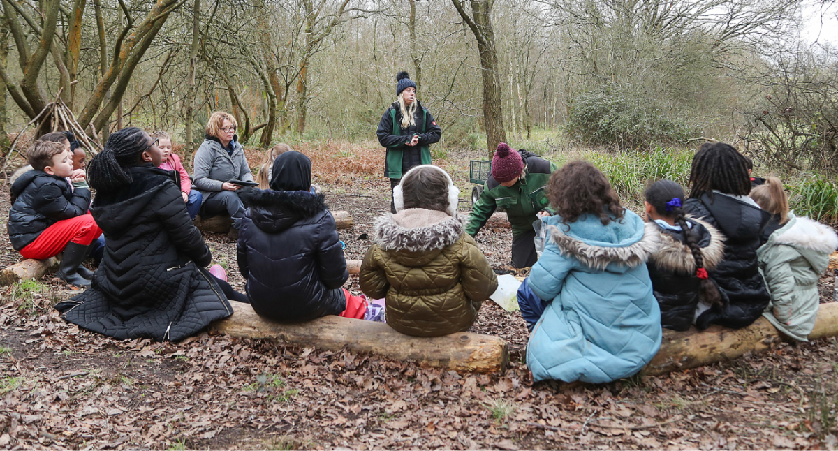 Ellie talking to a school group who are sitting on logs in a semi-circle shape.