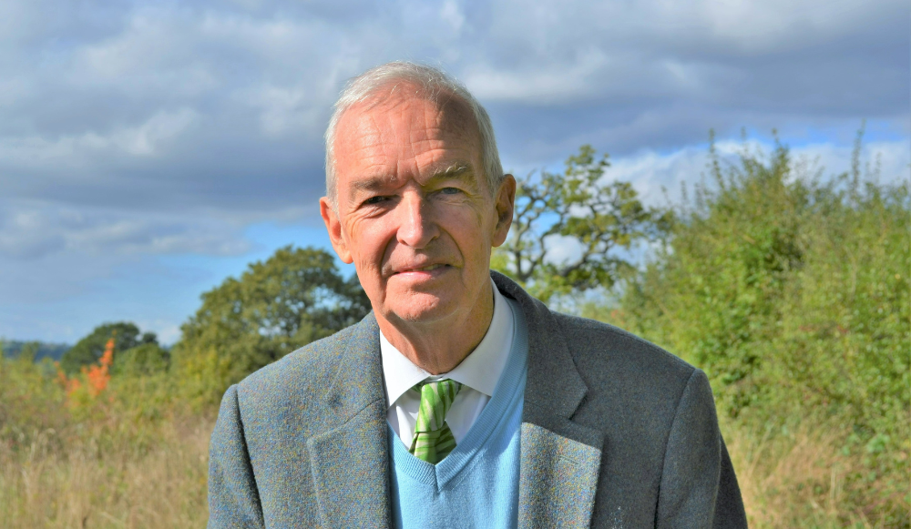 A head and shoulders photo of Jon Snow taken with grass and trees in the background. Heather is smiling at the camera