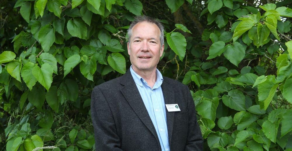 A head and shoulders photo of Neil Darlison standing in front of a background of green leaves