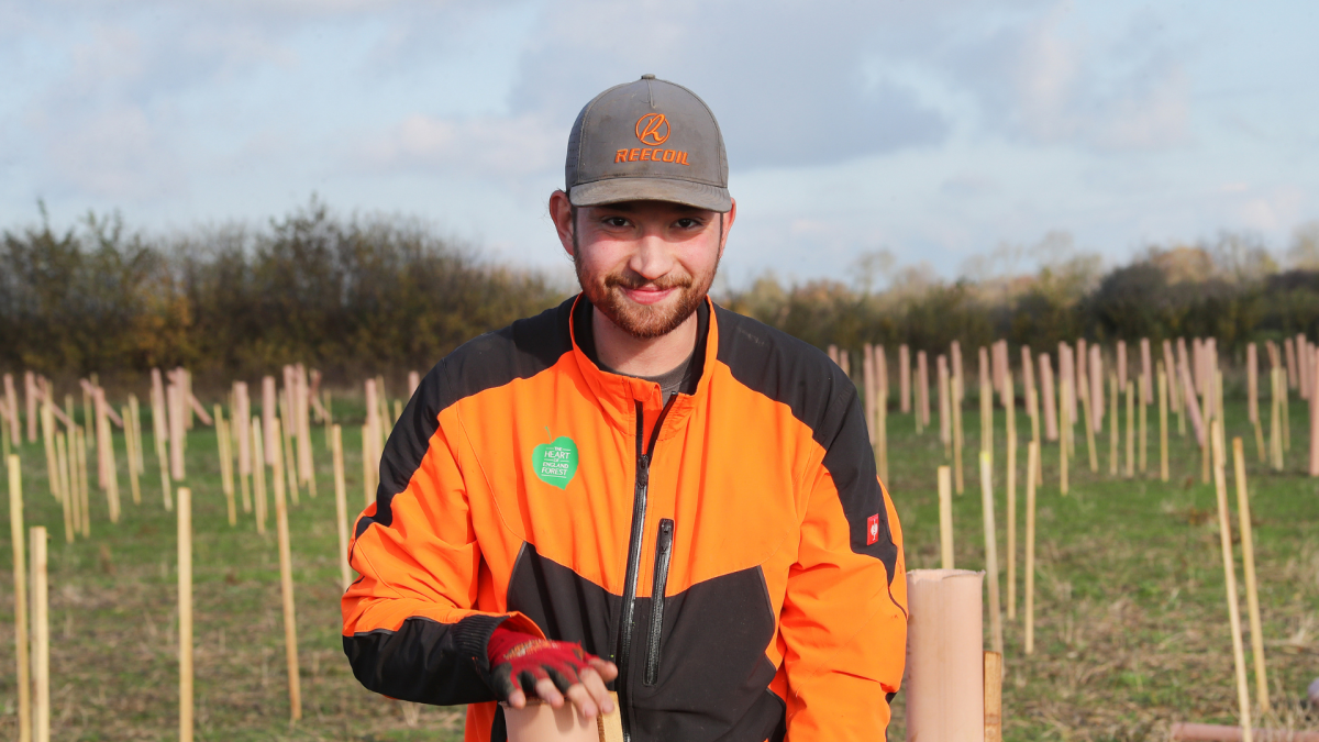 Member of our Forestry team, Hugo, is standing smiling at the camera with a new plantation behind him
