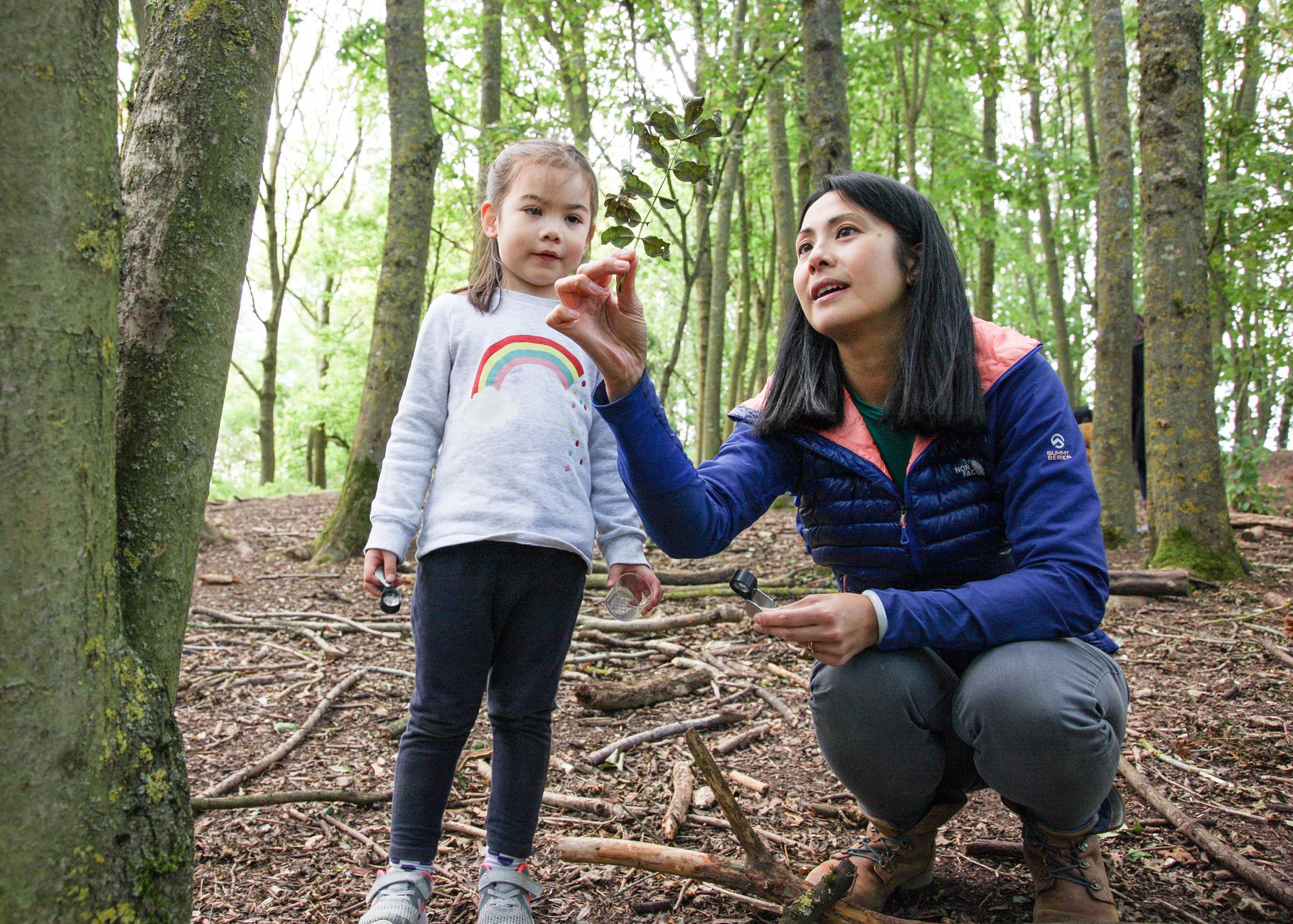 Child in the forest looking at a leaf with her mum